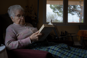 elderly woman sitting on a sofa reading a book