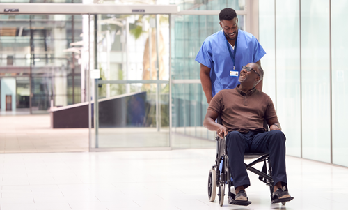 man seated in a transit wheelchair with a caregiver